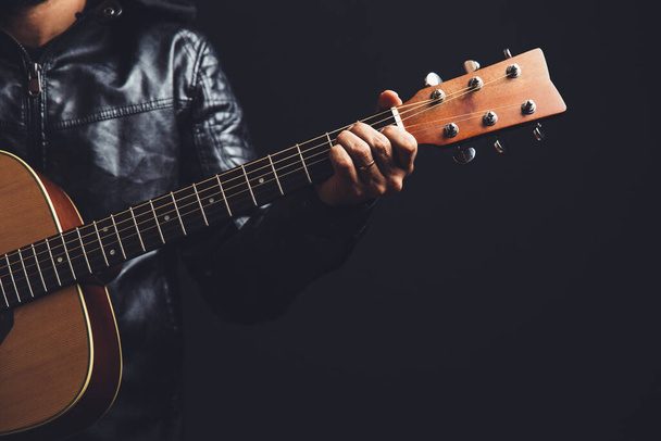 mężczyzna w skórzanej kurtce gra na gitarze akustycznej na czarnym tle - Zdjęcie, obraz