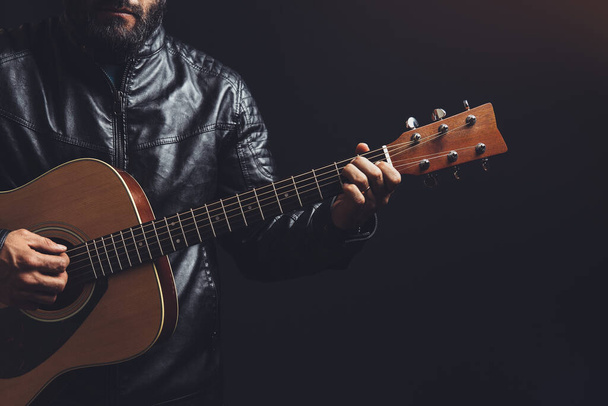 mężczyzna w skórzanej kurtce gra na gitarze akustycznej na czarnym tle - Zdjęcie, obraz