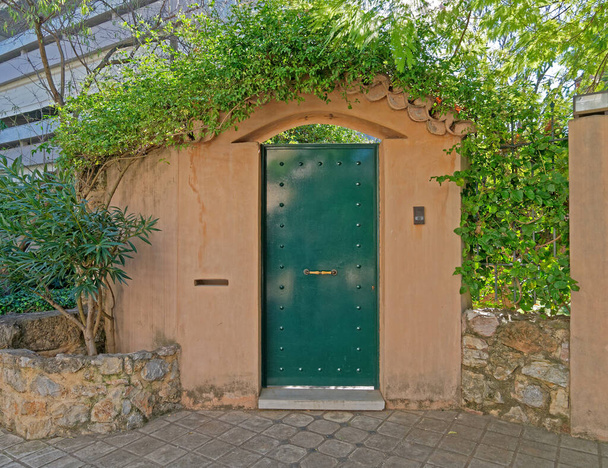 элегантный вход в дом металлическая зеленая дверь и ограда из охристой стены, из Греции - Фото, изображение
