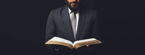человек в костюме с открытой библией на черном фоне - Фото, изображение