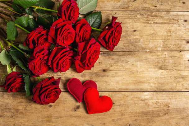 Bukiet świeżych burgundowych róż i miękkich serc filcowych na zabytkowym drewnianym tle. Pachnące czerwone kwiaty, pomysł na prezent na Walentynki, ślub lub urodziny, płaskie leżaki - Zdjęcie, obraz