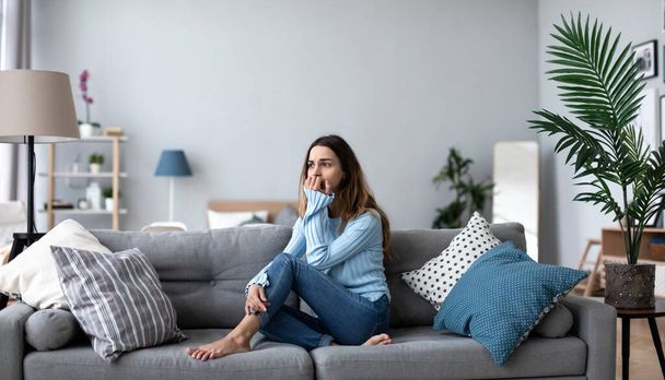 Upset young woman thinking about problem, sitting alone on couch at home, psychological problem. - Photo, image