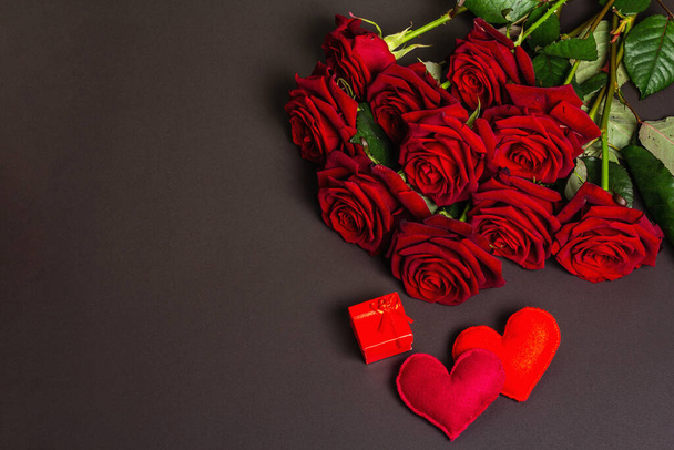 Μπουκέτο με φρέσκα τριαντάφυλλα μπορντό, δώρο και καρδιές από μαλακό τσόχα σε μαύρο φόντο από μπετόν. Αρωματικά κόκκινα λουλούδια, ιδέα για δώρο για την Ημέρα του Αγίου Βαλεντίνου, Γάμος ή Γενέθλια, επίπεδη lay - Φωτογραφία, εικόνα