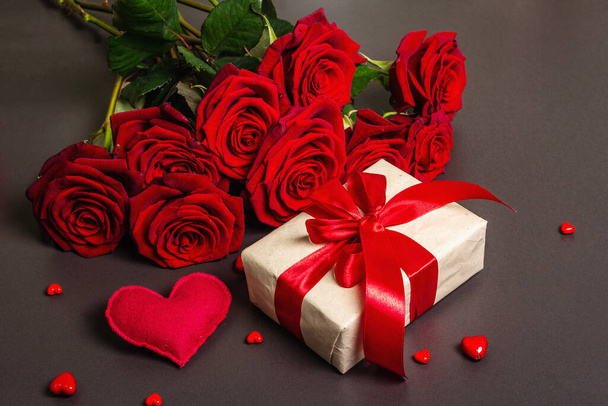 Bukiet świeżych burgundowych róż, prezentów i świątecznych serc na czarnym kamiennym tle betonowym. Pachnące czerwone kwiaty, pomysł na prezent na Walentynki, ślub lub urodziny, płaskie leżaki - Zdjęcie, obraz
