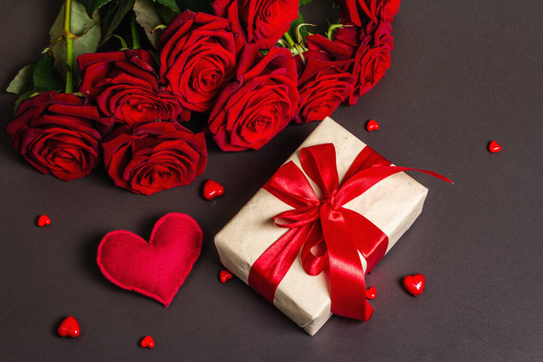 Μπουκέτο με φρέσκα τριαντάφυλλα μπορντό, δώρο και γιορτινές καρδιές σε φόντο από μαύρο μπετόν. Αρωματικά κόκκινα λουλούδια, ιδέα για δώρο για την Ημέρα του Αγίου Βαλεντίνου, Γάμος ή Γενέθλια, επίπεδη lay - Φωτογραφία, εικόνα