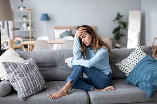 Грустная расстроенная женщина сидит на диване в гостиной одна дома, психологические проблемы.  - Фото, изображение