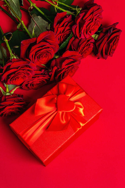 Friss burgundi rózsa csokor és ajándékdoboz matt vörös habirán háttérrel. Illatos vörös virágok, ajándék koncepció Valentin-nap, esküvő vagy születésnap - Fotó, kép
