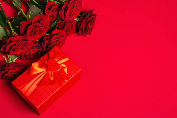 Bukiet świeżych burgundowych róż i pudełko prezentów na matowym czerwonym tle foamirańskim. Pachnące czerwone kwiaty, pomysł na prezent na Walentynki, ślub lub urodziny - Zdjęcie, obraz