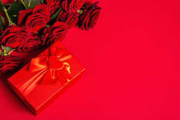 Bouquet frischer weinroter Rosen und Geschenkbox auf mattem rotem Schaumstoff-Hintergrund. Duftende rote Blumen, Geschenkkonzept für Valentinstag, Hochzeit oder Geburtstag - Foto, Bild