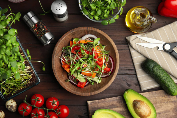 Salad with fresh organic microgreen in bowl and ingredients on wooden table, flat lay - Φωτογραφία, εικόνα
