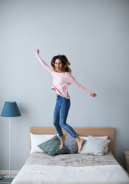 Happy young woman jumping on the bed at home. Good weekend. - Valokuva, kuva