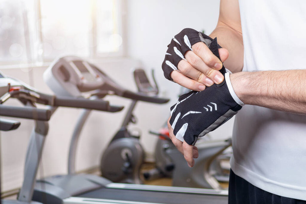 Sportovec nosí fitness rukavice na pozadí běžeckých pásem. - Fotografie, Obrázek