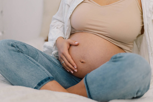 Atraktivní těhotná žena sedí v posteli a drží se za břicho. Koncepce těhotenství. - Fotografie, Obrázek