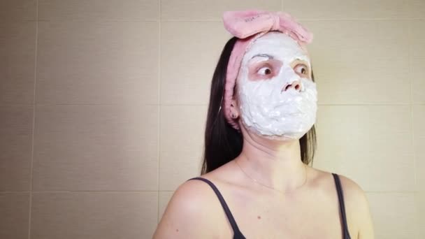 Молодая брюнетка с розовой ободкой наносит альгинатную маску на лицо с помощью косметической щетки. Процедуры ухода за кожей дома. - Кадры, видео