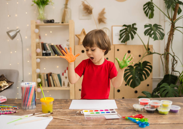 un bambino artista con le palme dipinte siede a un tavolo nella stanza - Foto, immagini