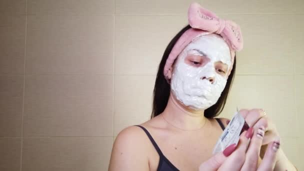 Joven morena con diadema rosa aplicando máscara de alginato en la cara usando cepillo cosmético. Procedimientos de cuidado de la piel en casa. - Metraje, vídeo
