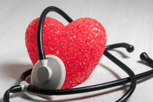 The big red heart is wrapped in a stethoscope. The concept of medical care, and cardiology. - Fotoğraf, Görsel
