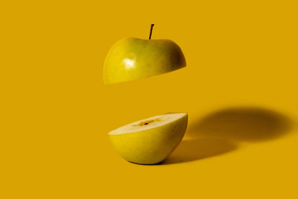Yeşil elma ikiye bölünmüş, yarısı havada yüzüyor. Koyu sarı arka plan. Yaratıcı meyve kavramı - Fotoğraf, Görsel
