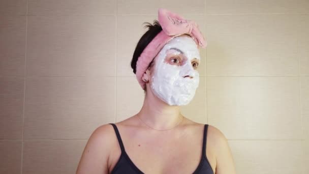 Молода брюнетка з рожевою пов'язкою наносить маску алкінату на обличчя за допомогою косметичної щітки. Процедури догляду за шкірою вдома
. - Кадри, відео