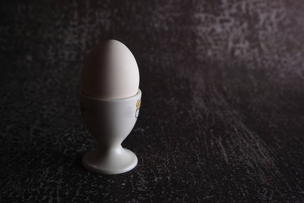 Варене біле одиночне великоднє яйце з тримачем на темному тлі
 - Фото, зображення