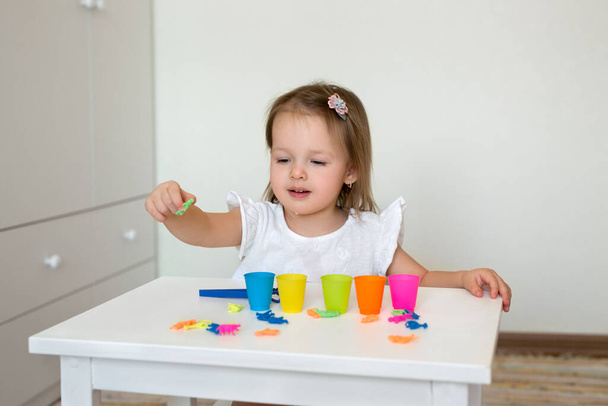 Дитина вчить кольори. Маленька дівчинка сортує фігури тварин за кольором, кидаючи їх у відповідну чашку. Розвиток дрібних моторних навичок
. - Фото, зображення