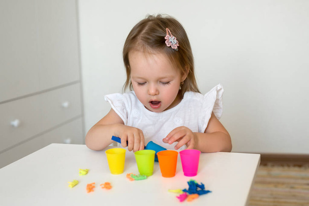 Dziecko uczy się kolorów. Mała dziewczynka sortuje figurki zwierząt według koloru, wrzucając je do odpowiedniego kubka. Rozwój umiejętności motorycznych. - Zdjęcie, obraz