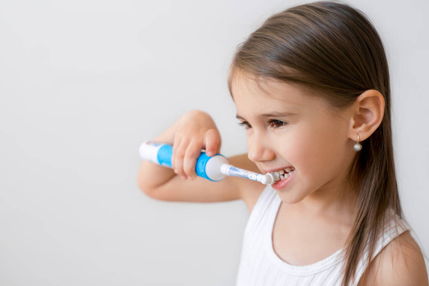 Child brushing teeth with electric toothbrush on white background. Dental hygiene. Copy space. Healthy baby teeth - Photo, Image