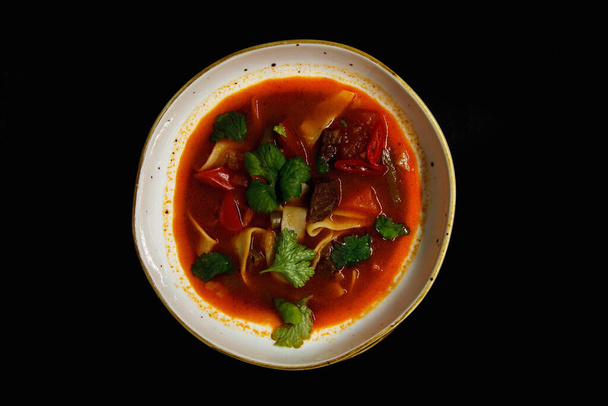 Spicy soup in a deep plate on a black background - Foto, afbeelding