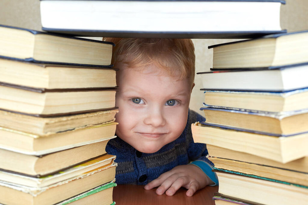 Mały, trzyletni, zabawny chłopiec patrzy z stosu książek.. - Zdjęcie, obraz