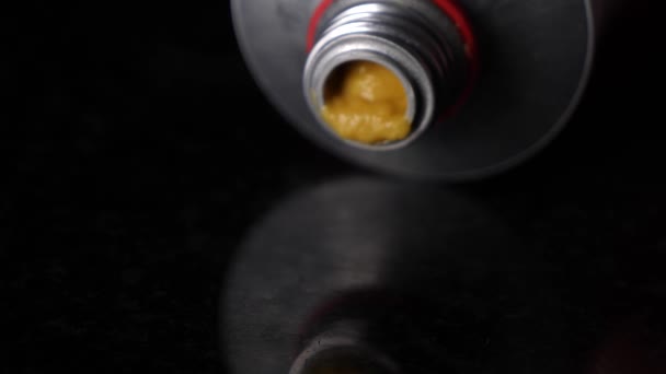Close up pressing mustard out of a tube on black reflective table. - Footage, Video