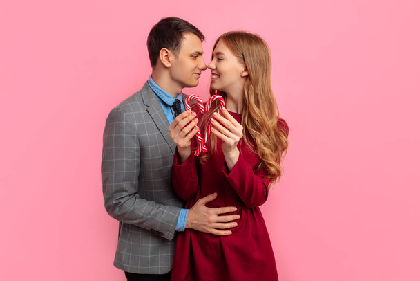 Valentine's day concept, happy young couple, with christmas striped sweets, making a heart on isolated pink background, valentines day - Fotoğraf, Görsel