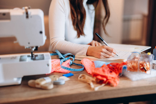 Young dressmaker woman is writing down ideas close-up. Creating online clothing design courses. - Photo, image
