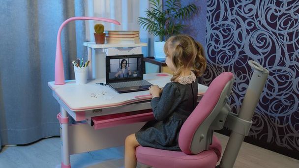 Детская дошкольная девочка дистанционное онлайн образование на дому, ученик смотрит видео уроки на ноутбуке - Фото, изображение