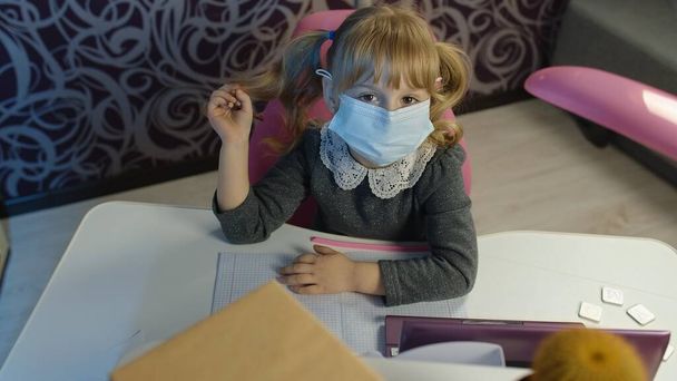 Kindermädchen Kind in medizinischer Maske macht Hausaufgaben am Laptop zu Hause, Fernunterricht - Foto, Bild