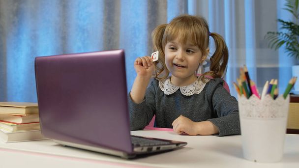 Tyttö tekee verkossa kotitehtäviä opettajan kanssa, digitaalisen kannettavan tietokoneen avulla kotona, etäopetus - Valokuva, kuva
