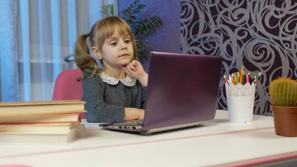 Çocuk okulu öğrenen kız, evde uzaktan eğitim laptopla masada oturuyor. - Fotoğraf, Görsel