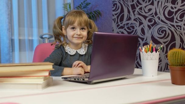 Детская девочка делает домашнее задание пишет в блокноте, с помощью ноутбука компьютер на дому, онлайн образование - Фото, изображение