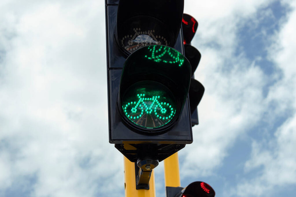 Крупный план зеленого светофора рядом с автомобильным светофором на перекрестке велосипедной дорожки с голубым облачным небом на заднем плане. - Фото, изображение