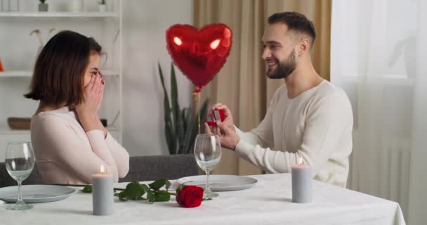 Couple having dinner at home celebrating valentines day anniversary, loving caring Caucasian husband gives gift with diamond ring to his beloved woman, boyfriend makes proposal for marriage, marry me - Footage, Video