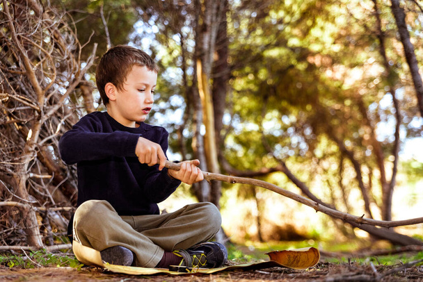 Egy gyermek ül a földön egy erdőben használja a botot, hogy rajzoljon a földre és megtapasztalja a természetet.. - Fotó, kép