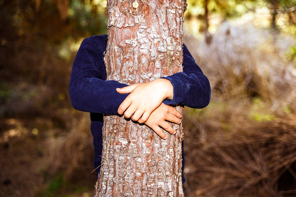 Bambino che abbraccia un albero in una foresta buia, prendendosi cura del pianeta. - Foto, immagini