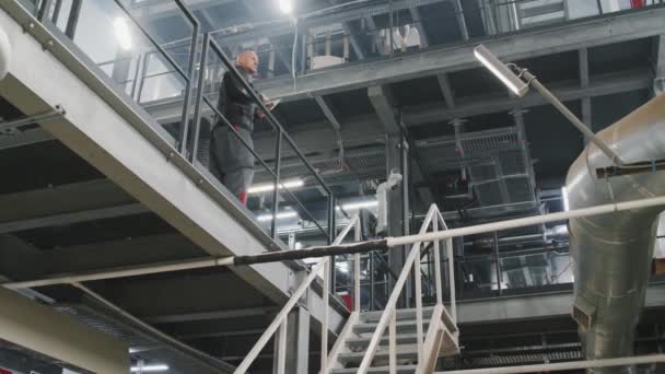 Plan complet au ralenti à faible angle de l'ouvrier caucasien adulte en combinaison contrôlant le processus de production dans une grande usine - Séquence, vidéo