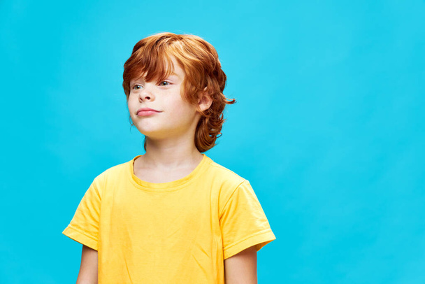 Roztomilý chlapec při pohledu na straně žluté tričko oříznuté pohled modré pozadí  - Fotografie, Obrázek