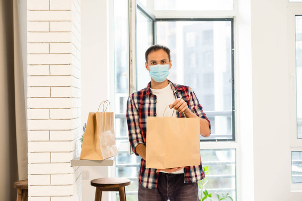 Entrega hombre sosteniendo bolsa de papel con comida, entrega de comida hombre en máscara protectora - Foto, imagen