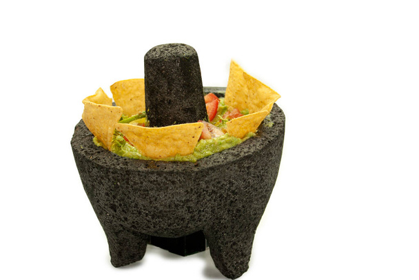 Salsa de aguacate adornada con chips de tortilla en un tazón de piedra acompañado de tomates rojos - Foto, Imagen