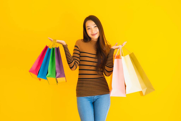 Portrait belle jeune femme asiatique sourire heureux avec beaucoup de couleur sac à provisions de grand magasin sur fond jaune isolé
 - Photo, image