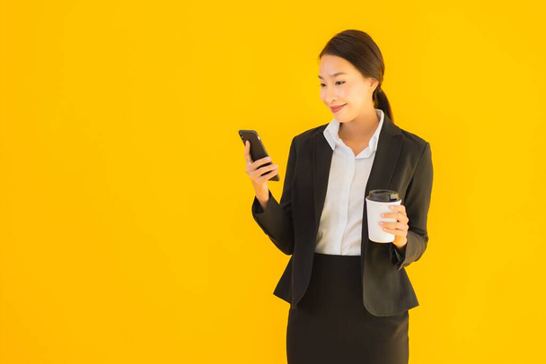Retrato hermosa joven negocio asiático mujer con teléfono móvil inteligente y taza de café en amarillo aislado fondo
 - Foto, imagen