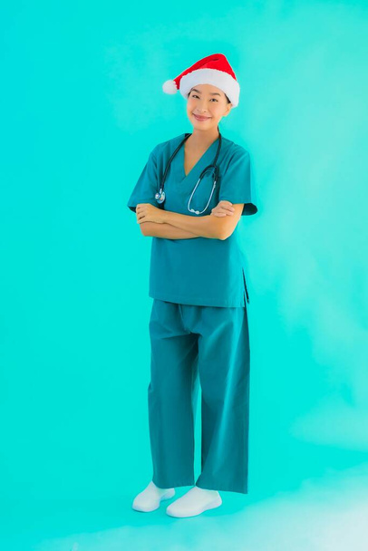 Portret piękny młody Azji lekarz kobieta nosić Boże Narodzenie kapelusz z uśmiechem szczęśliwy na niebieskim odosobnionym tle - Zdjęcie, obraz