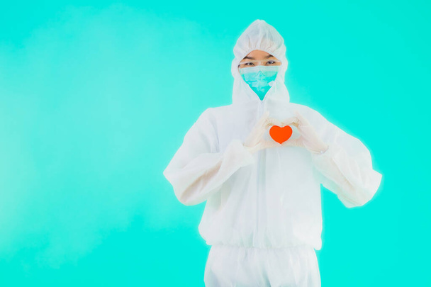 Retrato hermosa joven asiática médico mujer usar ppe o equipo de protección personal para proteger de coronavirus o covid19 mostrar el corazón en azul aislado fondo
 - Foto, Imagen