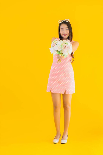 Retrato hermosa joven asiática mujer con colorido flor en amarillo aislado fondo
 - Foto, Imagen